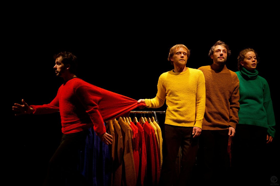 Quatre interprètes en pulls rouge, jaune, brun et vert, l'un tirant sur une manche démesurément étirée.