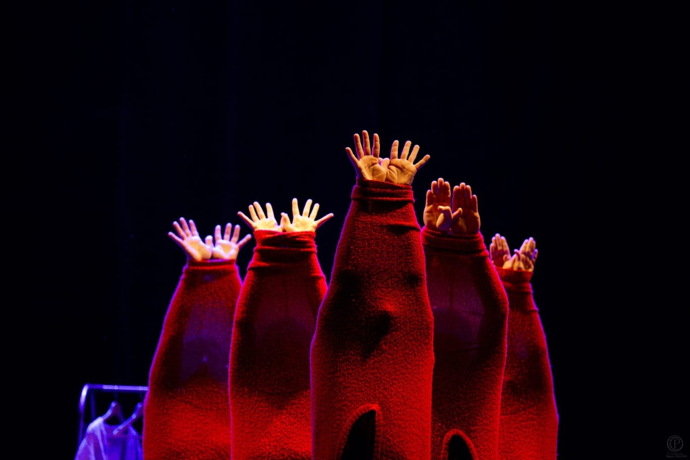 Des mains surgissent de pulls de laine rouge dressés sur une scène noire — visuel du spectacle ImPulls.